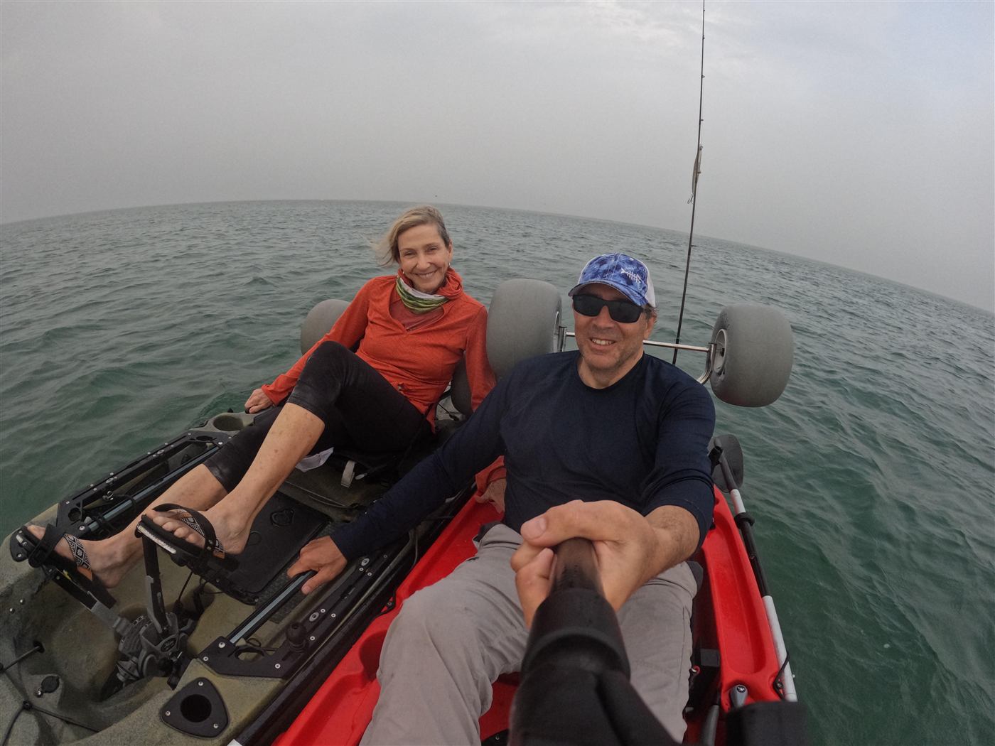 Two kayakers side by side on open ocean under an overcast sky
